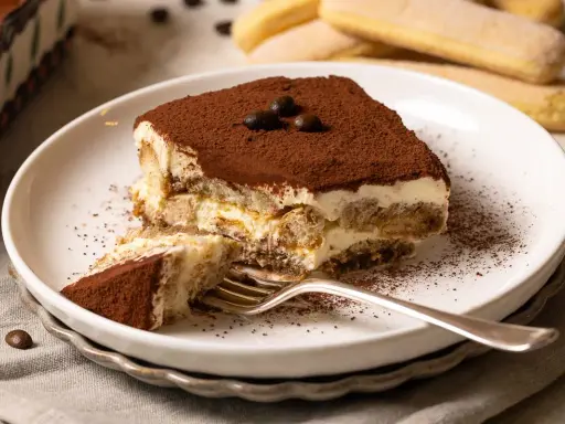 Ein Stück cremiges Tiramisu, bestäubt mit Kakao, wartet auf dich. Dieses Tiramisu Rezept ist ein Genuss!