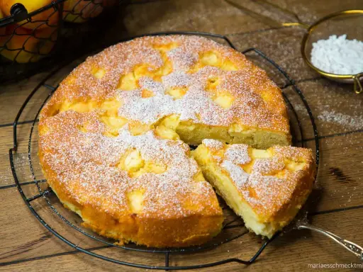 Omas weltbester Apfelkuchen, frisch gebacken und mit Puderzucker bestäubt, wartet auf seine Genießer. Ein Stück ist bereits herausgeschnitten.