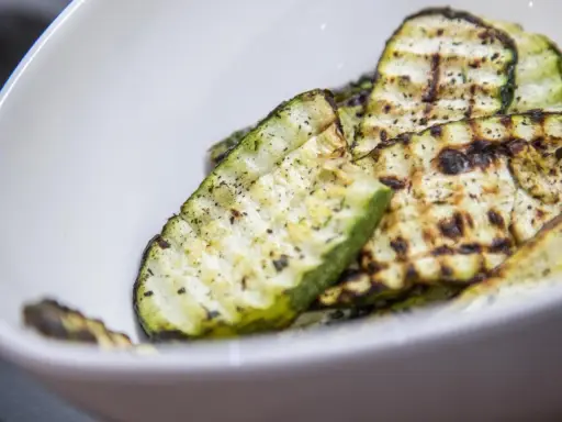 Gegrillte Zucchinischeiben mit Kräutern und Gewürzen in einer weißen Schüssel. Eine köstliche Zucchini Pfanne.