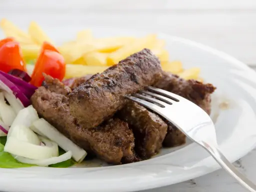 Saftige cevapcici mit knusprigen Pommes, garniert mit frischem Salat, Tomaten und Zwiebeln. Ein köstliches Gericht!