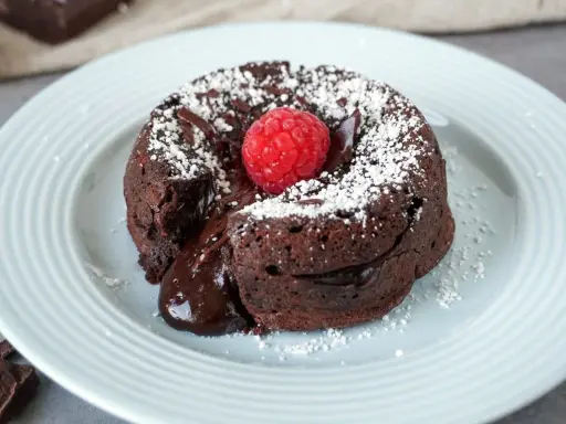 Ein warmer Schokoladenkuchen, ein Coulant de Chocolate, mit flüssigem Kern, garniert mit einer Himbeere und Puderzucker.