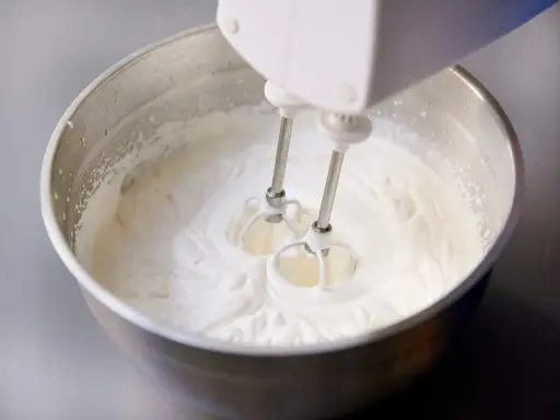 Ein Handmixer schlägt Kochsahne in einer Edelstahlschüssel zu steifer Masse.