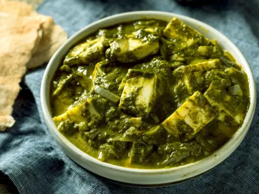 Schüssel mit cremigem Palak Paneer, einem indischen Gericht aus Spinat und Käse, daneben Fladenbrot.