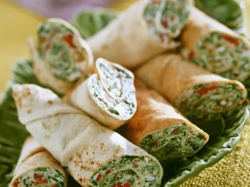 Gerollte Tortilla-Wraps mit Spinat und Feta, appetitlich auf einem grünen Blatt serviert.