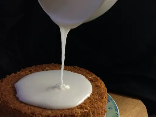 Ein Kuchen wird mit zuckerguss mit milch überzogen. Der flüssige Guss fließt langsam auf die runde Kuchenoberfläche.