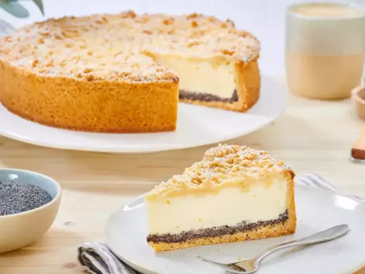 Ein köstlicher Mohn Schmand Kuchen mit Streuseln und Puderzucker. Daneben eine Schale Mohn und eine Tasse Kaffee.