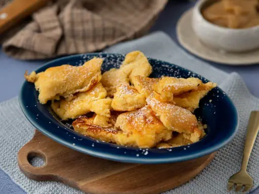 Kaiser­sch­marrn, ein Klassiker der besten Thermomix Rezepte, bestäubt mit Puderzucker auf einem blauen Teller.