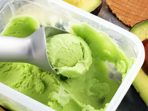 Cremiges, grünes veganes Eis, perfekt zum veganes Eis selber machen mit Mandelmilch. Avocados und Waffeln im Hintergrund.