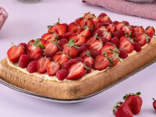 Ein rechteckiger Biskuit-Erdbeerkuchen vom Blech, üppig belegt mit frischen Erdbeeren und Himbeeren auf einer cremigen Schicht.