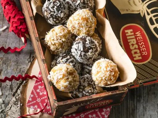 Leckere energy balls selber machen! Eine Mischung aus dunklen und hellen Kugeln, umhüllt von Kokosraspeln, in einer alten Blechdose.