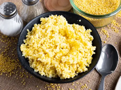 Goldhirse kochen: Ein Teller mit dampfender Hirse, daneben Salz- und Pfefferstreuer, Löffel und eine Schüssel voller ungekochter Hirse.