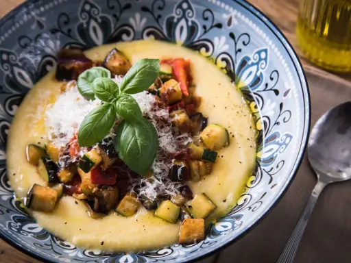 Cremige Polenta mit gebratenem Gemüse, Parmesan und Basilikum. So ist Polenta genau richtig: ein herzhaftes Gericht, das wärmt.