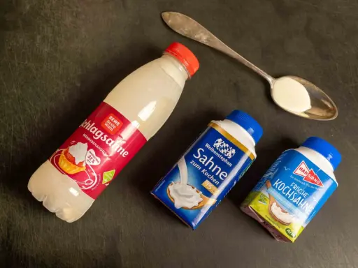 Schlagsahne zum Kochen: verschiedene Sahne-Produkte liegen neben einem Löffel mit Sahne.