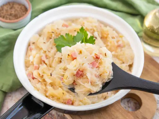 Herzhaftes Sauerkraut nach Hausfrauenart mit Speck und Kümmel, garniert mit Petersilie. Ein Löffel voller Tradition.