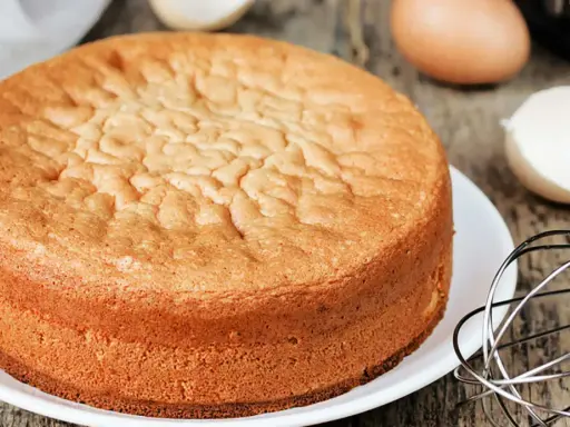 Ein goldbrauner Biskuitboden, perfekt für jedes biskuitboden rezept. Eier und Schneebesen deuten auf die Zubereitung hin.