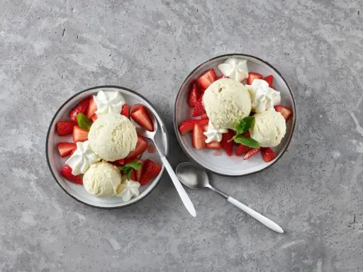 Zwei Schalen mit Erdbeeren Romanoff: frische Erdbeeren, cremiges Eis und Schlagsahne, garniert mit Minze.