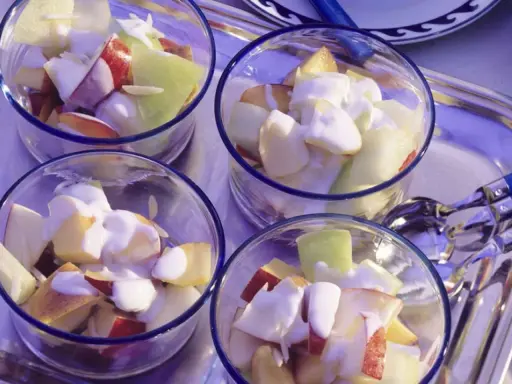 Vier Gläser mit einem erfrischenden Nachtisch mit griechischem Joghurt und Obststücken.