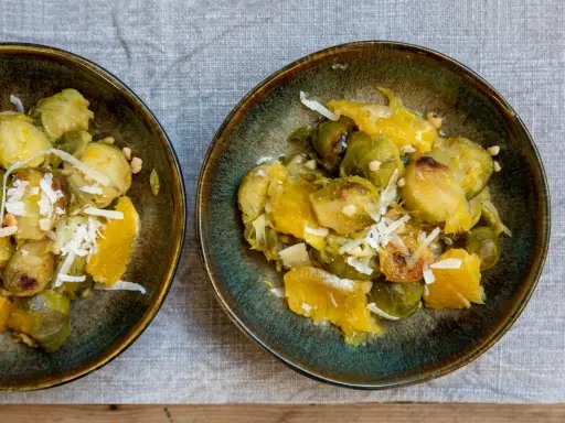 Zwei Schalen mit Rosenkohl, Orangenstücken und geriebenem Käse. Ein Gericht, das an ewiger Kohl Rezepte erinnert.