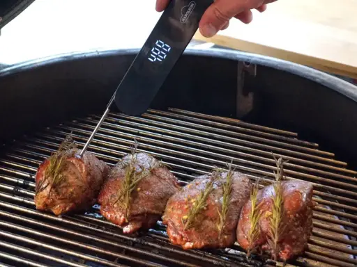 Vier Hirschsteaks mit Rosmarin auf dem Grill, ein Thermometer zeigt 48°C an. So gelingt das Hirschsteak richtig braten.