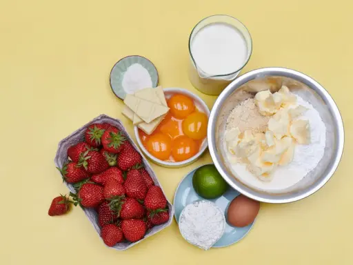 Zutaten für eine Erdbeerspiegel Torte: Erdbeeren, Eigelb, weiße Schokolade, Butter, Mehl, Zucker, Milch, Ei, Limette und Backpulver.