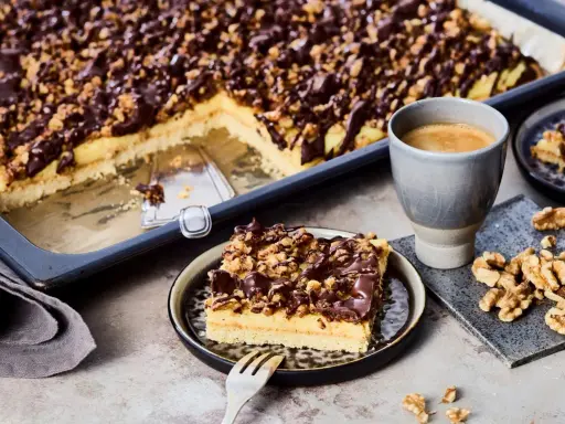 Ein Stück "friss dich dumm Kuchen" mit Schokoladen-Nuss-Decke und einer Tasse Kaffee.