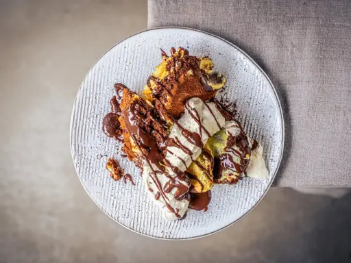 Ein köstlicher Somlauer Nockerl-Dessert auf einem Teller, mit Schokoladensauce und Eiscreme garniert.