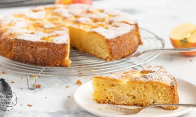 Ein saftiger glutenfreier Apfelkuchen, bestäubt mit Puderzucker, auf einem Gitterrost. Ein Stück auf einem Teller mit Gabel daneben.