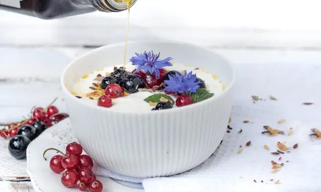 Joghurt mit Beeren und leinsamen, beträufelt mit Honig. Blaue Kornblumen zieren die Schüssel.