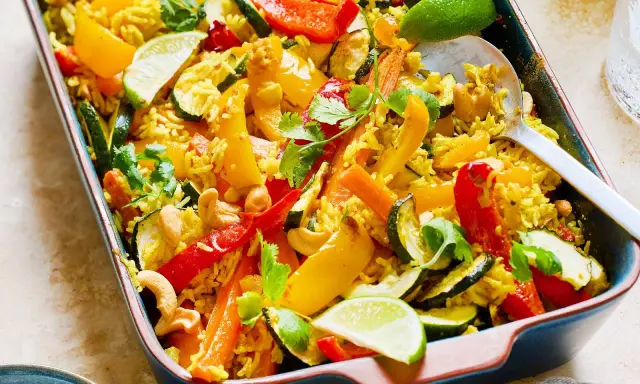 Buntes Gericht mit Reis, Paprika, Zucchini, Karotten und Cashewkernen, garniert mit Koriander und Limettenspalten. Ein köstliches Gericht mit Reis für jeden Anlass.