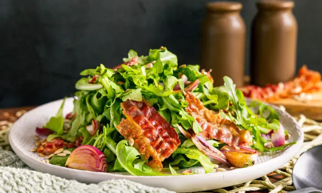 Salat mit Rucola, roten Zwiebeln und knusprigem Speck. Perfekte warme Beilagen zum Salat, die für zusätzlichen Geschmack sorgen.