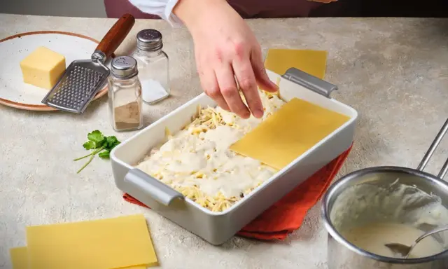 Hände legen Lasagneplatten auf eine Schicht Käse und Sauce. Ein Schritt im Lasagne rezept.