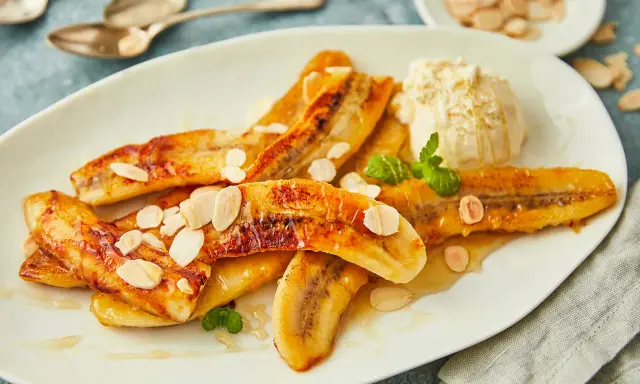 Gebackene Bananen mit einer Kugel Eis, garniert mit Mandelblättchen und Minze. Ein süßer Genuss!