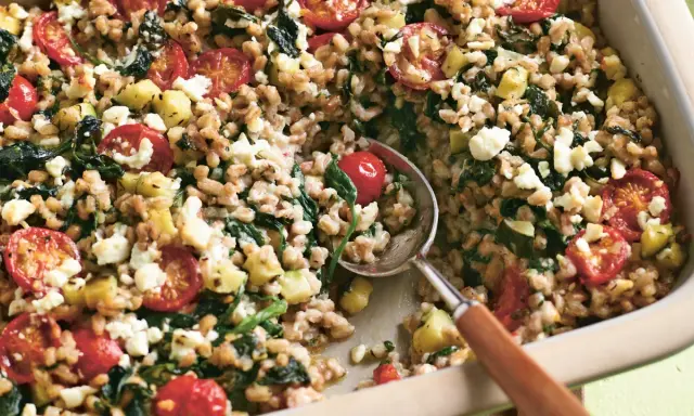 Herzhaftes Gericht mit gekochtem Dinkel, Tomaten, Zucchini und Feta. Ein Löffel hebt die köstliche Mischung aus der Auflaufform.