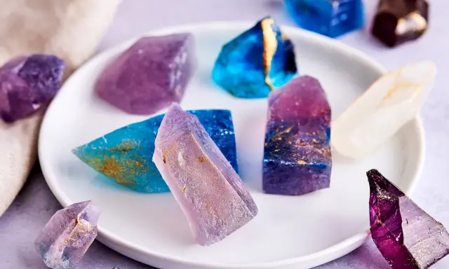 Bunte, essbare Kristalle selber machen: glitzernde Zuckerstücke in Blau, Lila und Weiß mit goldenen Akzenten auf einem Teller.