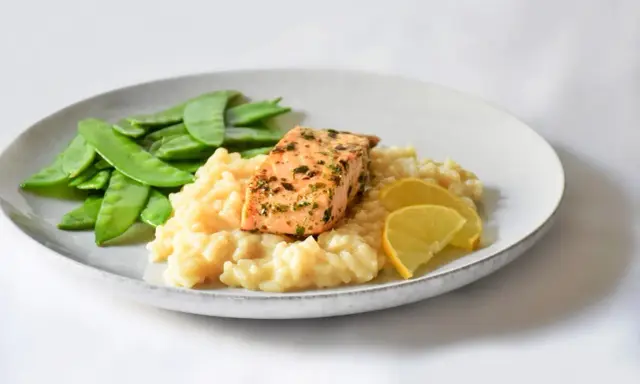 Ein Stück Lachs auf cremigem Zitronenrisotto, garniert mit Zuckerschoten und Zitronenspalten.