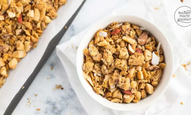 Schüssel mit selbstgemachtem, gesundem Granola, Nüssen und Kokosflocken. Daneben ein Blech mit frisch gebackenem Müsli.
