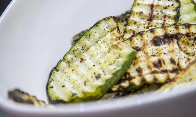 Gegrillte Zucchinischeiben mit Kräutern und Gewürzen in einer weißen Schüssel. Eine köstliche Zucchini Pfanne.