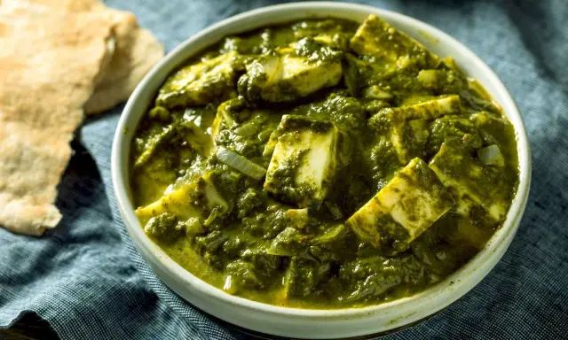 Schüssel mit cremigem Palak Paneer, einem indischen Gericht aus Spinat und Käse, daneben Fladenbrot.