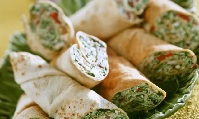 Gerollte Tortilla-Wraps mit Spinat und Feta, appetitlich auf einem grünen Blatt serviert.