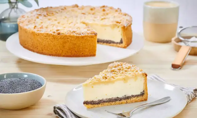 Ein köstlicher Mohn Schmand Kuchen mit Streuseln und Puderzucker. Daneben eine Schale Mohn und eine Tasse Kaffee.