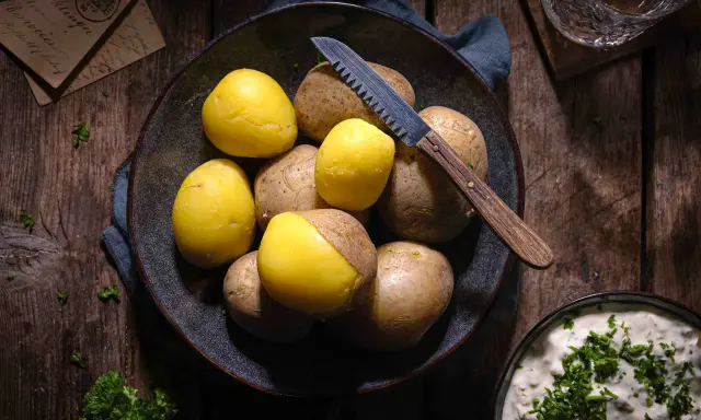 Gekochte und rohe Kartoffeln liegen in einer Schale, bereit für ein deftiges Essen. Ein Messer mit Holzgriff liegt daneben.