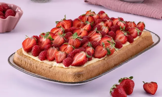 Ein rechteckiger Biskuit-Erdbeerkuchen vom Blech, üppig belegt mit frischen Erdbeeren und Himbeeren auf einer cremigen Schicht.