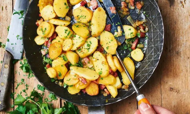 Bratkartoffeln mit mehligen Kartoffeln, Speck und Zwiebeln in einer Pfanne, garniert mit Petersilie.