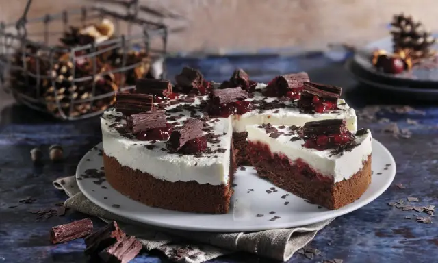 Schokoladen-Sahne-Torte mit Preiselbeeren und Schokostückchen, dekoriert mit Schokoraspeln. Ein Stück ist angeschnitten.