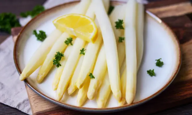 Frischer weißer Spargel, perfekt gegart, liegt auf einem Teller, garniert mit Petersilie und einer Zitronenspalte.