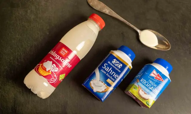 Schlagsahne zum Kochen: verschiedene Sahne-Produkte liegen neben einem Löffel mit Sahne.