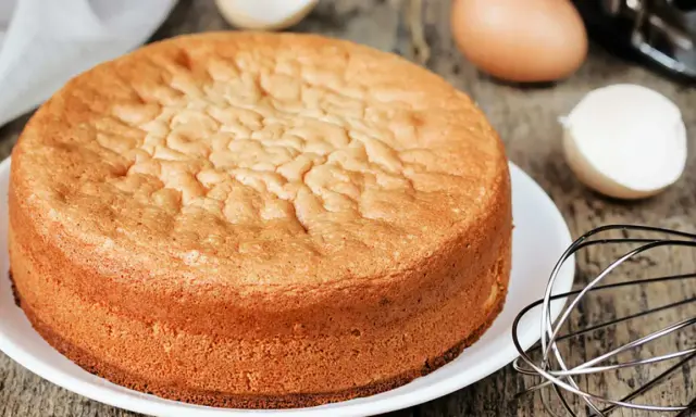 Ein goldbrauner Biskuitboden, perfekt für jedes biskuitboden rezept. Eier und Schneebesen deuten auf die Zubereitung hin.