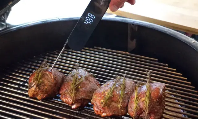 Vier Hirschsteaks mit Rosmarin auf dem Grill, ein Thermometer zeigt 48°C an. So gelingt das Hirschsteak richtig braten.
