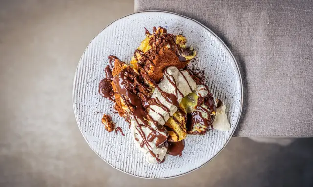 Ein köstlicher Somlauer Nockerl-Dessert auf einem Teller, mit Schokoladensauce und Eiscreme garniert.