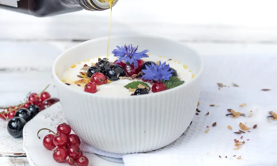 Joghurt mit Beeren und leinsamen, beträufelt mit Honig. Blaue Kornblumen zieren die Schüssel.